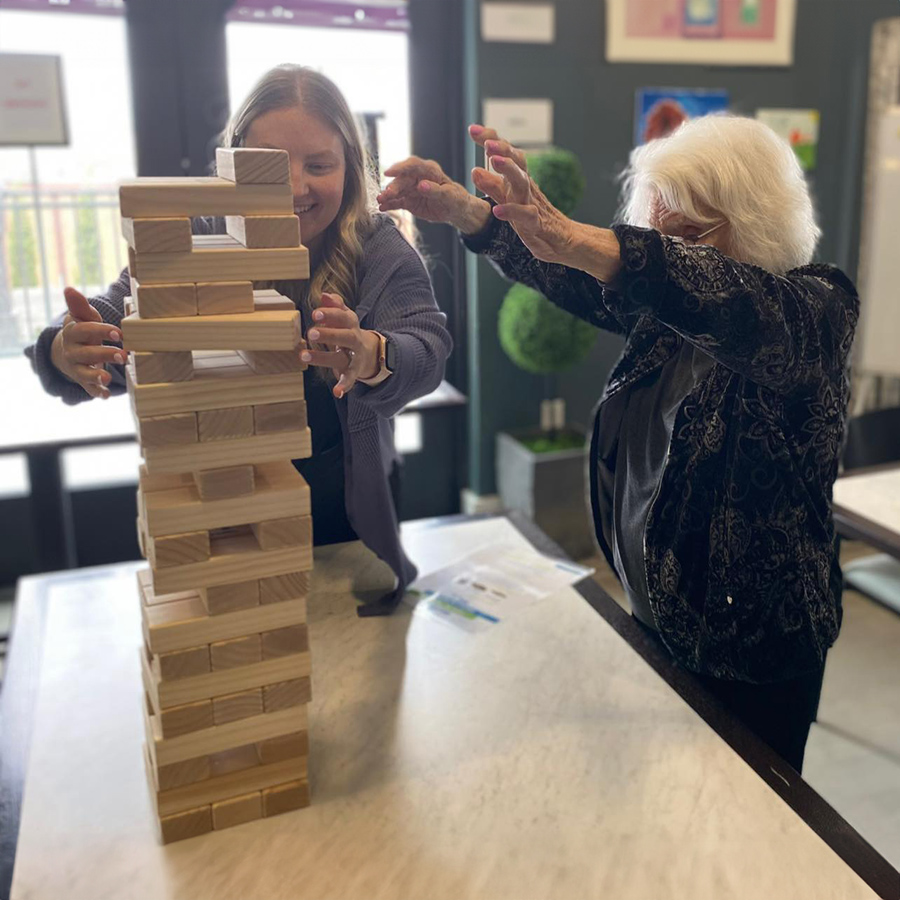 Joyful senior living residents bond over a thrilling game of wooden tower "Jenga" in a warm and inviting room with an employee.
