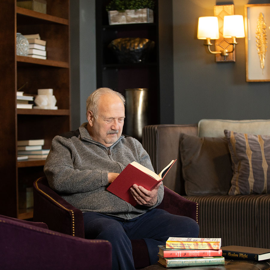 Elderly man reading book in Town and Country Senior Living library.