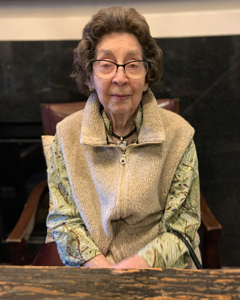 A current photo of Barbara in glasses, a soft beige vest, and a green blouse.