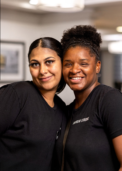 Two smiling team members at Arrow Senior Living posing together, showcasing the positive and friendly work environment that fosters collaboration and strong relationships.